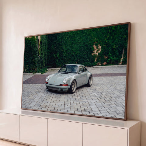 Porsche 911 clássico cinza-esverdeado em piso de pedras diante de muro coberto de hera, quadro decorativo