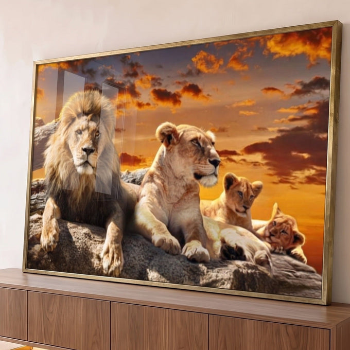 Leão, leoa e dois filhotes deitados em rocha sob céu laranja de pôr do sol, quadro decorativo
