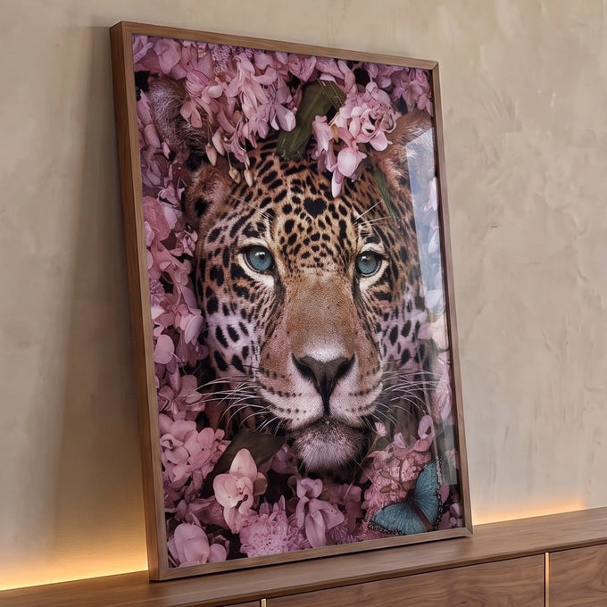 Rosto de onça pintada com olhos azuis cercado por flores rosas e folhas verdes, quadro decorativo