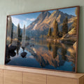Lago de montanha espelhando picos iluminados pelo sol, pinheiros e pedras sob céu azul, quadro decorativo