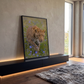 Leopardo agachado à espreita, olhar intenso, em campo verde com flores lilás, quadro decorativo