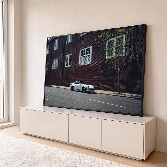 Porsche 911 clássico branco estacionado em rua diante de prédio de tijolos vermelhos, quadro decorativo