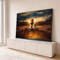 Leão caminhando em riacho ao pôr do sol com reflexo dourado na água e montanhas, quadro decorativo
