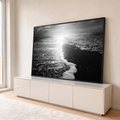 Fotografia em preto e branco de espuma do mar na areia escura com sol refletindo, quadro decorativo
