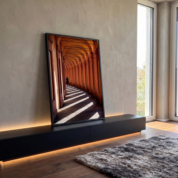 Corredor de arcos terracota com faixas de luz e sombra e pessoa caminhando ao fundo, quadro decorativo