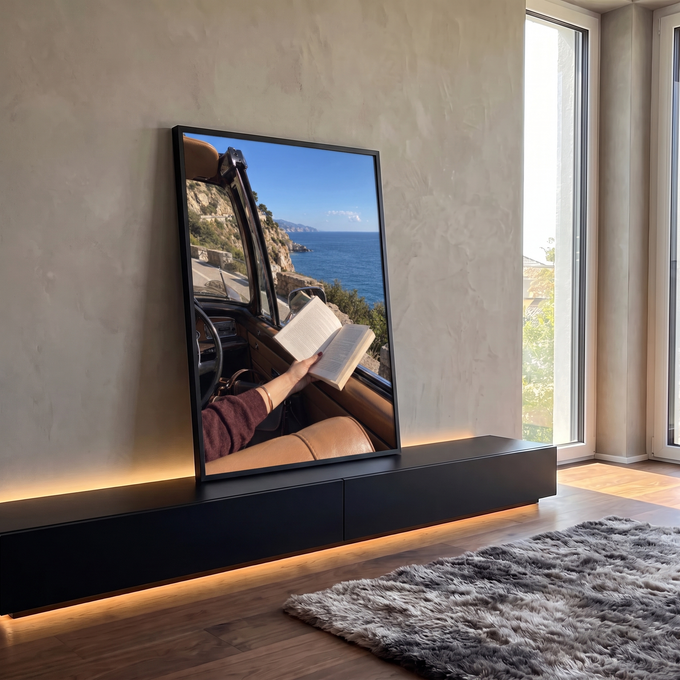 Mão segurando livro aberto em carro conversível retrô, estrada à beira-mar azul, quadro decorativo