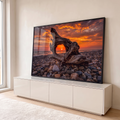 Tronco de madeira emoldurando o pôr do sol laranja sobre o mar em praia de seixos, quadro decorativo