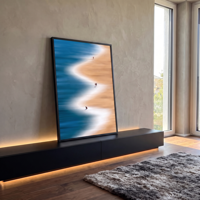 Praia vista do alto com mar azul, espuma branca em zigue-zague e pessoas na areia, quadro decorativo