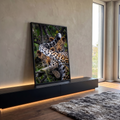 Dois filhotes de leopardo deitados em galho de árvore com folhas verdes ao fundo, quadro decorativo