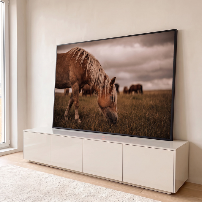 Cavalo de crina loira pastando em campo com manada ao fundo e céu nublado, quadro decorativo