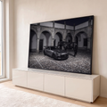 Carro esportivo cinza e cavalo negro em pátio de pedra com arcos coloniais à noite, quadro decorativo