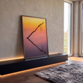 Galho seco em silhueta refletido em água calma sob céu laranja, rosa e lilás, quadro decorativo