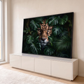 Rosto de onça-pintada com olhos âmbar espreitando entre folhas de monstera e palmeiras, quadro decorativo