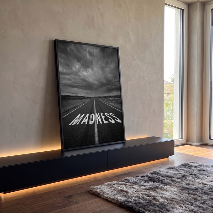 Estrada com a palavra MADNESS pintada no asfalto sob céu tempestuoso em preto e branco, quadro decorativo