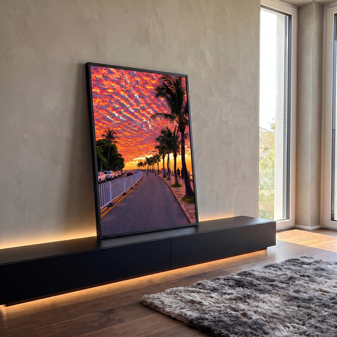 Pôr do sol laranja e vermelho sobre orla com palmeiras, ciclistas e mar ao fundo, quadro decorativo