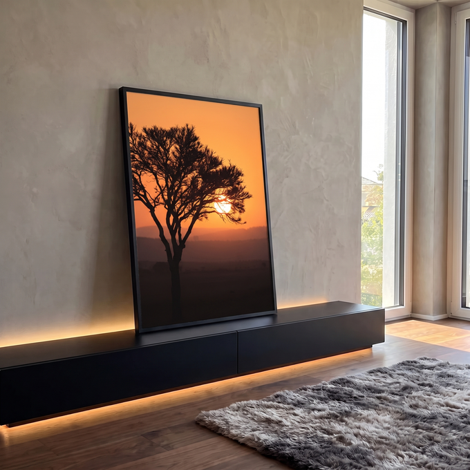 Árvore em silhueta com sol entre os galhos em céu laranja sobre colinas enevoadas, quadro decorativo