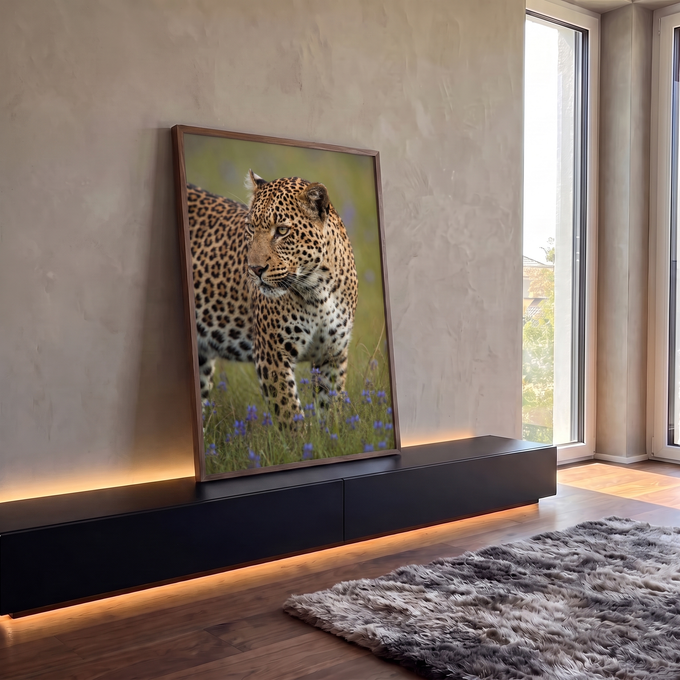 Leopardo em close olhando de lado, entre flores roxas em campo verde, quadro decorativo