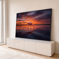 Flamingo rosa caminhando em lago calmo com reflexo na água sob céu laranja de pôr do sol, quadro decorativo