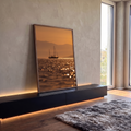 Veleiro em silhueta sobre mar cintilante ao pôr do sol laranja com montanhas, quadro decorativo