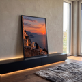 Gato branco e gato preto em muro de pedra olhando o pôr do sol laranja sobre o mar, quadro decorativo