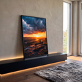 Banco de madeira em colina diante de rio sob pôr do sol laranja e nuvens escuras, quadro decorativo