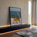Mulher de terno xadrez e cabelo platinado com poltrona amarela e TV retrô à beira-mar, quadro decorativo