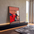 Mulher loira de vestido preto e salto alto encostada em carro esportivo vermelho, quadro decorativo