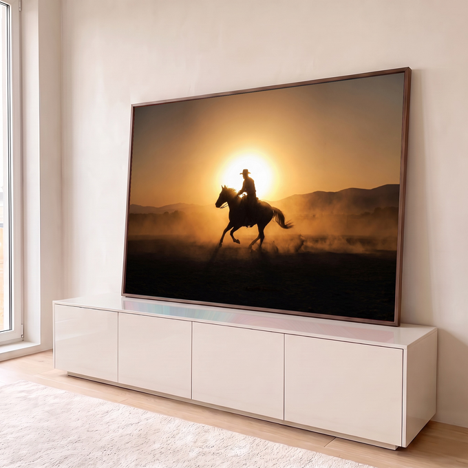 Silhueta de cowboy galopando a cavalo em contraluz ao pôr do sol com poeira dourada, quadro decorativo