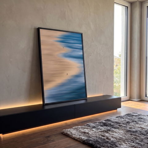 Praia vista do alto com mar azul em movimento, areia bege e duas pessoas caminhando, quadro decorativo