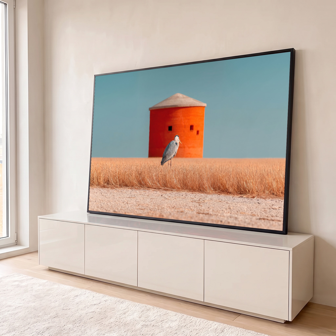 Garça cinzenta em campo de grama dourada diante de torre laranja sob céu azul, quadro decorativo