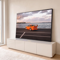 Porsche 911 laranja com aerofólio à beira-mar, skyline e céu nublado ao entardecer, quadro decorativo