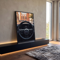 Volante de carro esportivo em couro preto com painel e prédios desfocados ao fundo, quadro decorativo