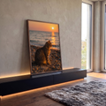 Gato tabby sentado em praia de pedras olhando o mar sob o sol poente alaranjado, quadro decorativo