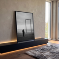 Senhor de casaco escuro olha o mar ao lado de moldura vazia na praia em preto e branco, quadro decorativo