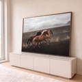 Três cavalos galopando na areia vulcânica com poeira, montanhas e céu nublado ao fundo, quadro decorativo