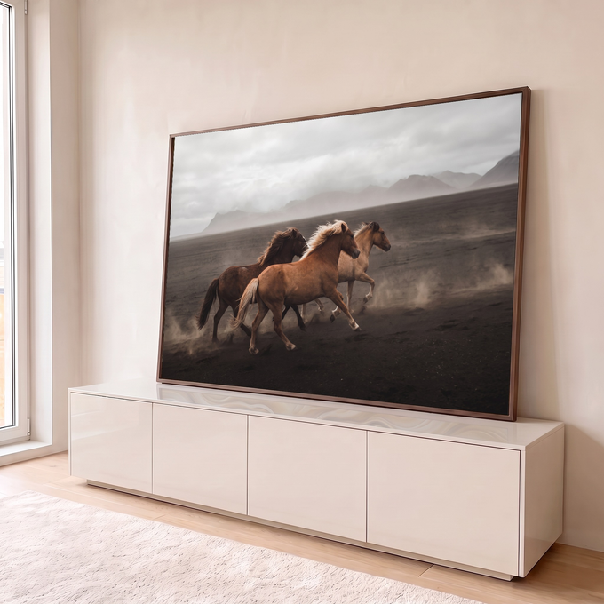 Três cavalos galopando na areia vulcânica com poeira, montanhas e céu nublado ao fundo, quadro decorativo