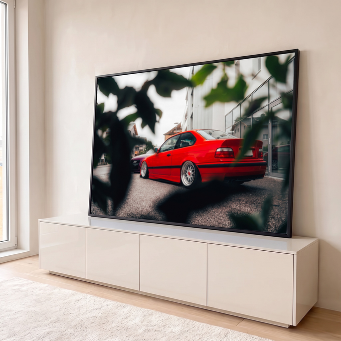 Carro esportivo vermelho rebaixado com rodas prateadas em rua entre folhas desfocadas, quadro decorativo