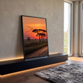 Pôr do sol laranja na savana com acácias em silhueta, pássaros voando e estrada de terra, quadro decorativo