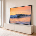 Surfista deslizando numa onda azul no mar ao pôr do sol, com céu laranja e reflexos dourados, quadro decorativo