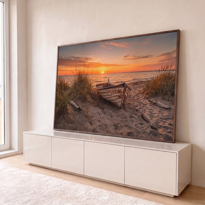 Barco de madeira rústico na areia entre capim de dunas com pôr do sol laranja no mar, quadro decorativo