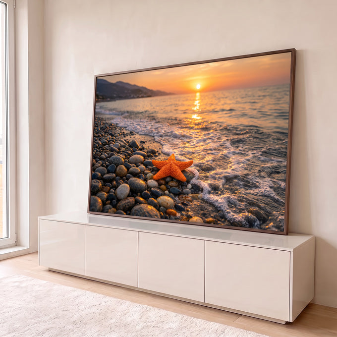Estrela-do-mar laranja sobre seixos na beira do mar com ondas e pôr do sol dourado ao fundo, quadro decorativo