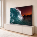 Onda do mar formando tubo azul-turquesa com céu laranja e prédios na orla ao entardecer, quadro decorativo