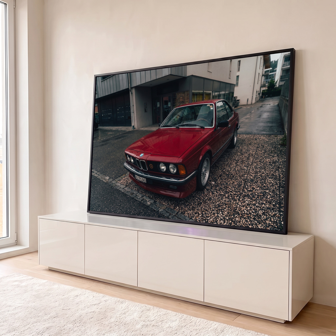 BMW coupé clássico vermelho estacionado em rua molhada com prédios cinza ao fundo, quadro decorativo