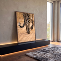 Close das patas e cauda malhada de leopardo caminhando sobre areia clara em tons bege, quadro decorativo