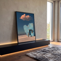 Casa azul em formato de coração na praia com homem, gato laranja e nuvem rosada, quadro decorativo