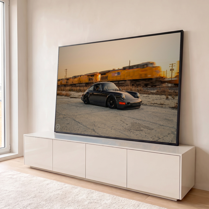 Porsche 911 preto rebaixado diante de trem de carga amarelo borrado sob céu de entardecer, quadro decorativo