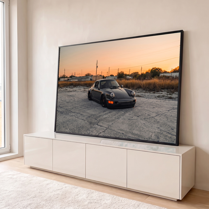 Porsche 911 preto rebaixado sobre concreto com céu alaranjado de pôr do sol, quadro decorativo