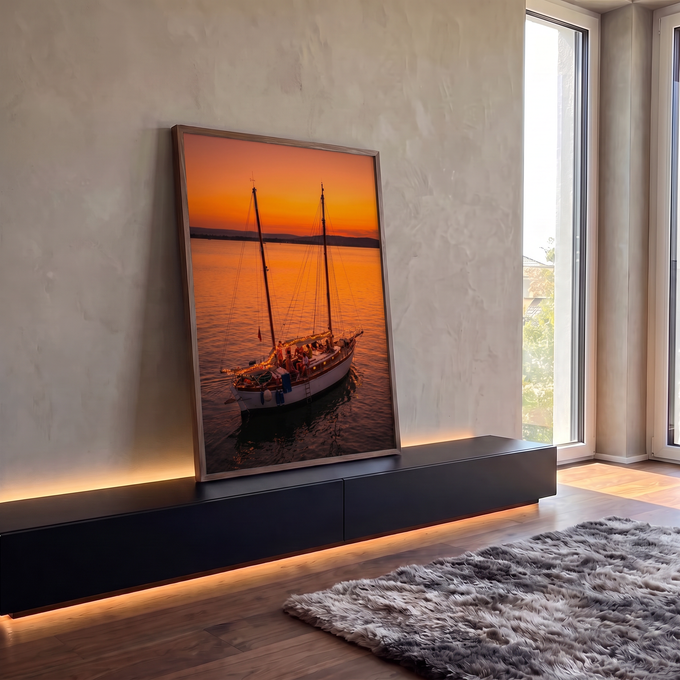 Veleiro com luzes e pessoas no convés navegando em mar calmo sob pôr do sol laranja, quadro decorativo
