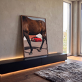 Ferrari F40 vermelha vista entre as patas de um cavalo marrom em pátio, quadro decorativo