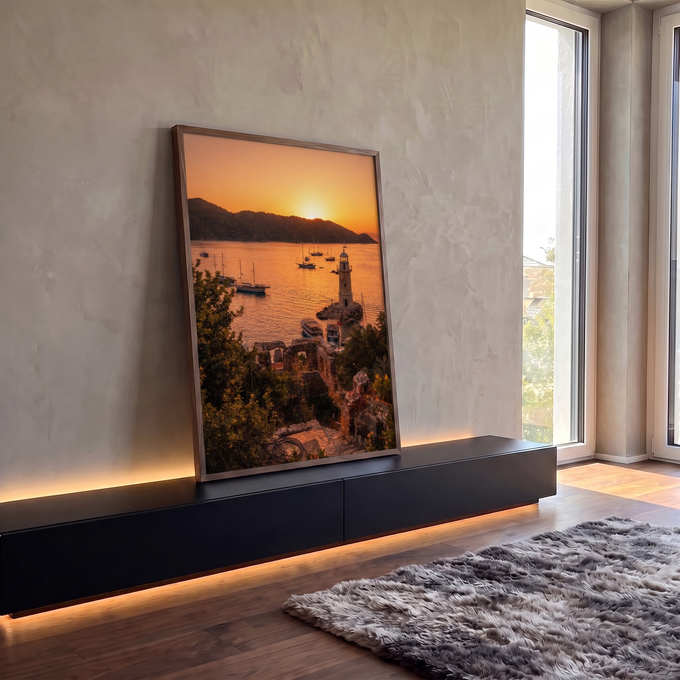 Farol de pedra e veleiros na baía ao pôr do sol laranja, com ruínas e vegetação, quadro decorativo